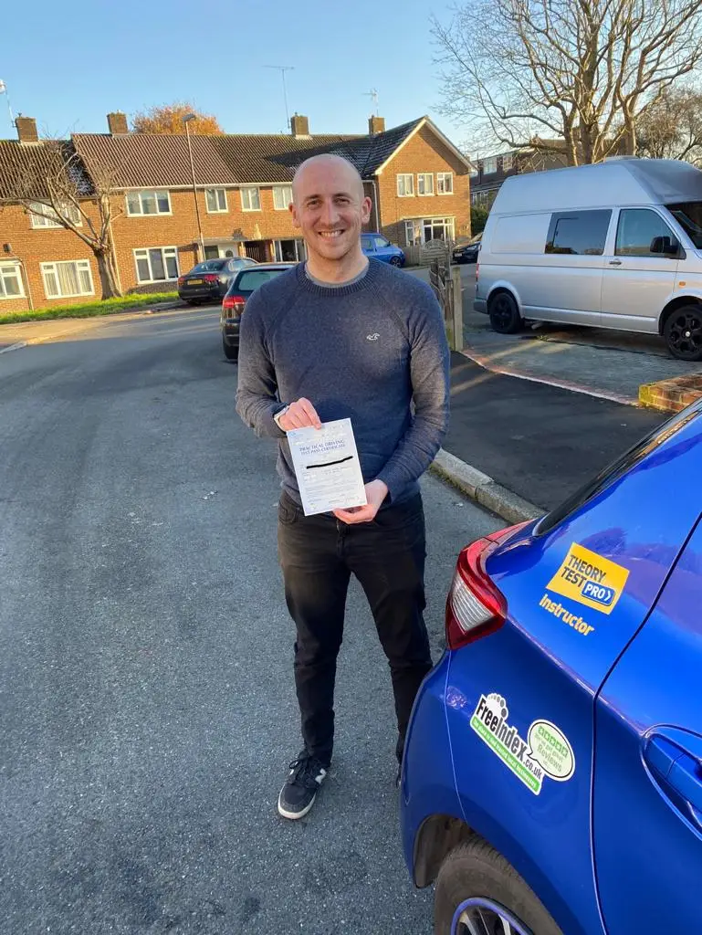 Learner holding his driving test pass certificate beside a car